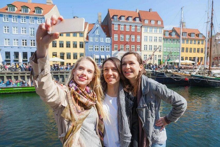 Three people taking a selfie with colorful buildings and boats in the background. 4