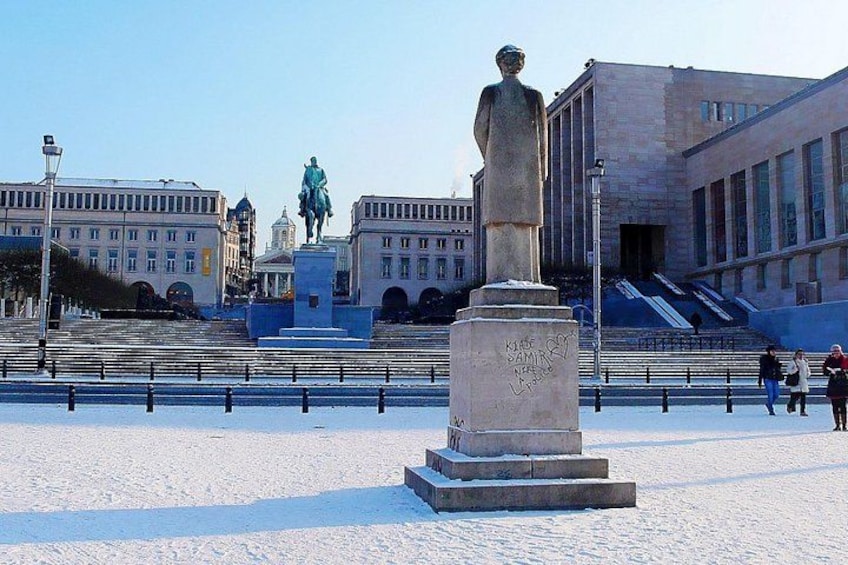 A statue in a square with steps leading up to it, surrounded by buildings and a clear sky. 2