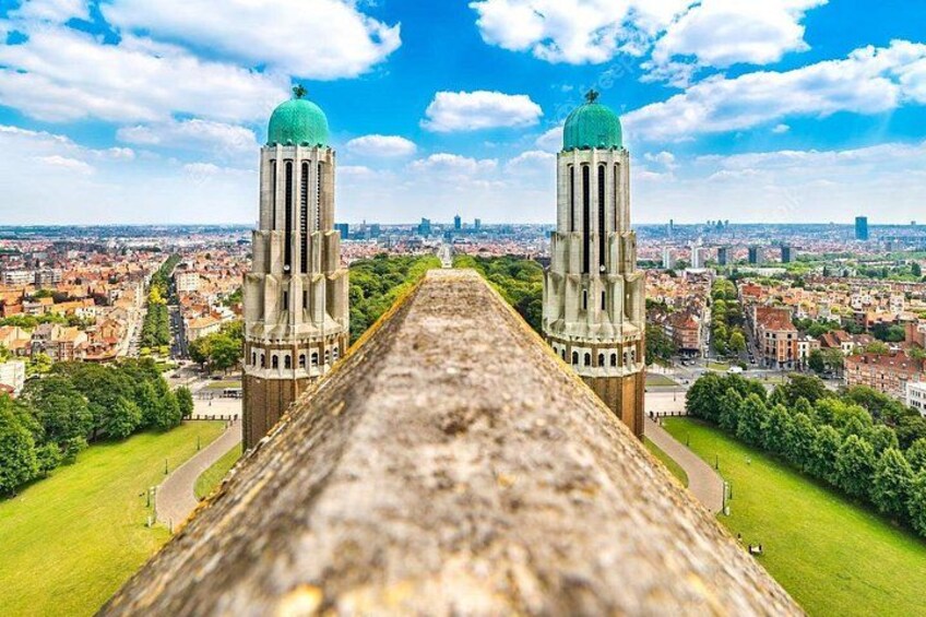 A long stone pathway leading to two towers with green domes, surrounded by a cityscape and greenery. 1