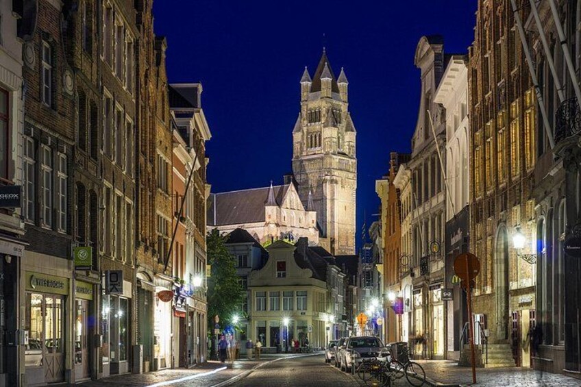 A nighttime street scene with historic buildings, a prominent clock tower, and a bicycle parked on the sidewalk. 2