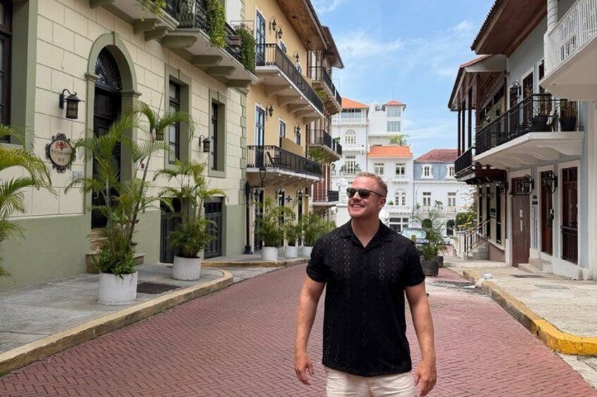 A man standing on a brick street with buildings on either side. 2