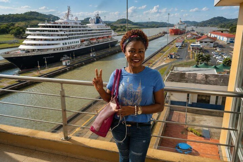 A person standing on a balcony overlooking a canal with a cruise ship and a docked ship in the background. 4