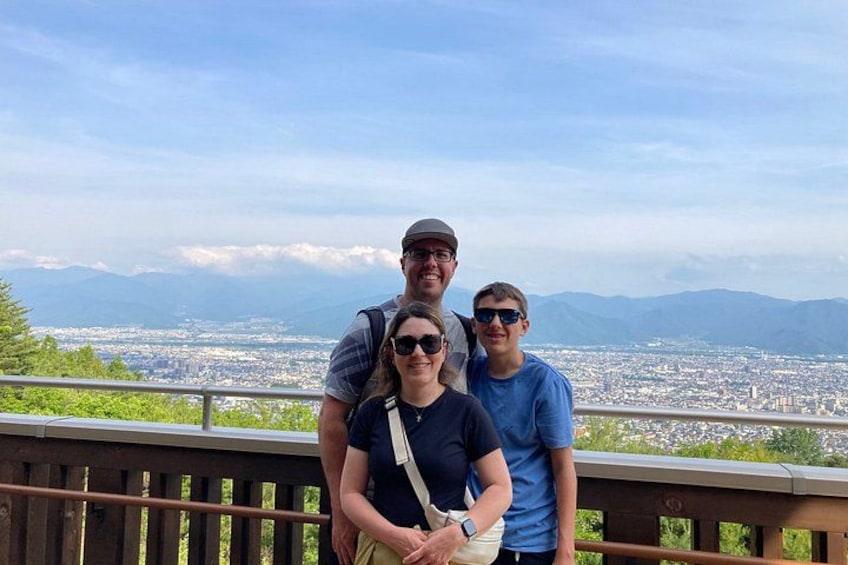 A group of people standing on a wooden deck overlooking a cityscape with mountains in the distance. 4