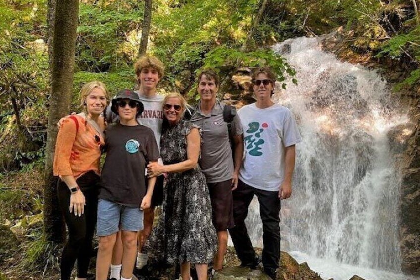 A group of people standing by a waterfall in a forested area. 1