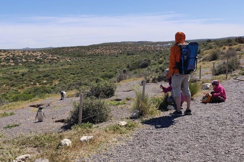 Una persona con una mochila sobre un camino de grava, otra sentada en el suelo, y una tercera caminando a lo lejos. 3