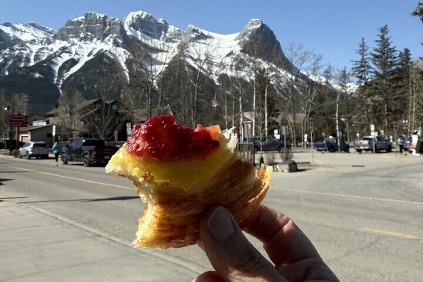 Una mano che tiene una ciambella con marmellata rossa con le montagne sullo sfondo. 1