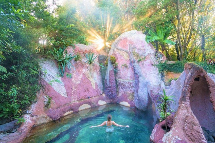 A person in a natural pool surrounded by rock formations and greenery. 1