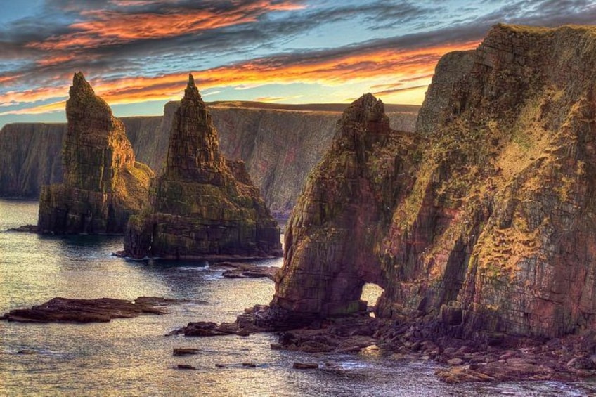 A coastal landscape with prominent rock formations and a sunset. 1