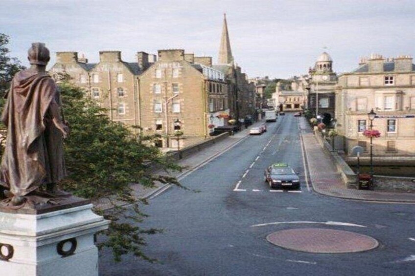 A street with a statue, buildings, and a roundabout. 4