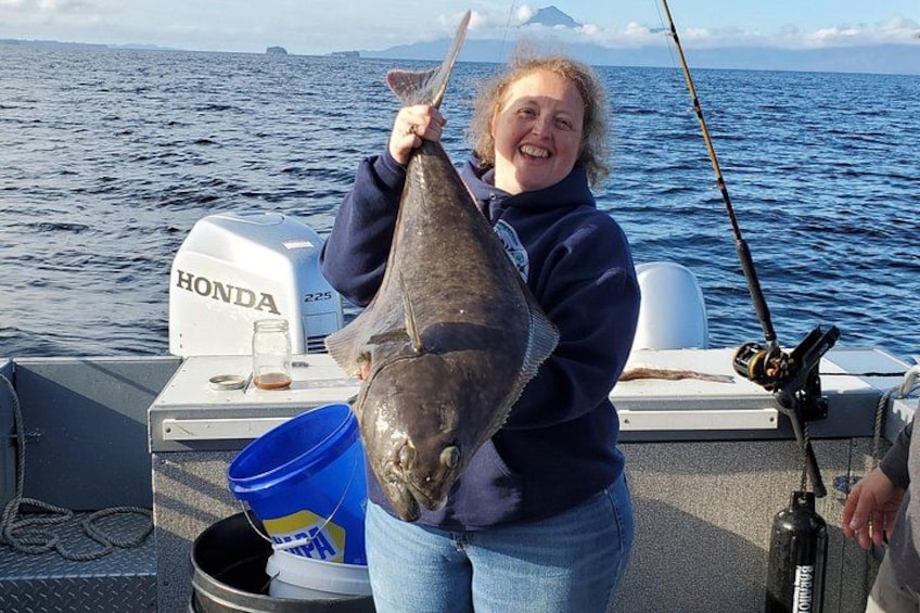 A person holding a large fish on a boat with a Honda outboard motor, a fishing rod, and a blue bucket. 1