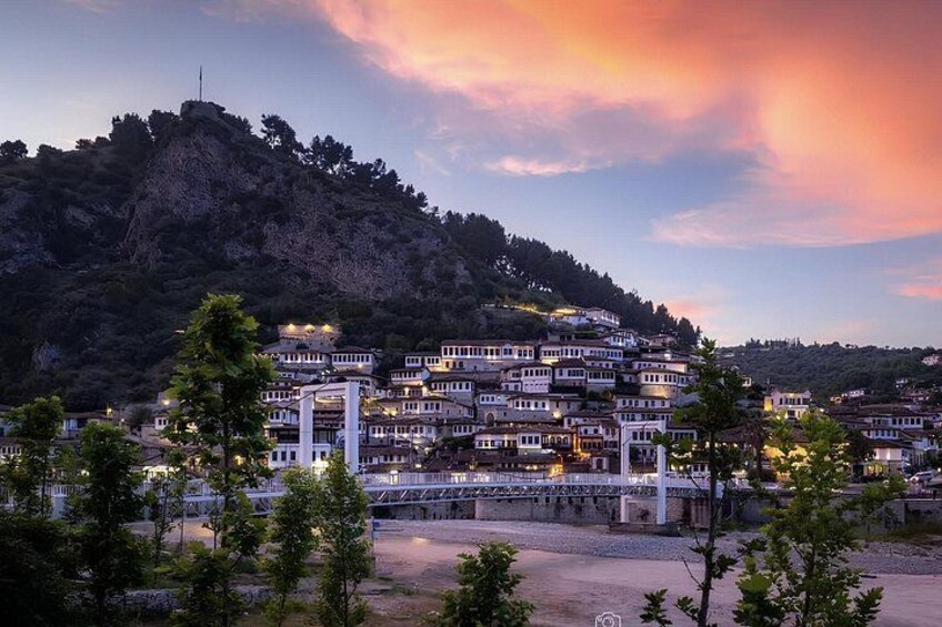A coastal town with terraced buildings, a bridge, and a hill in the background. 1