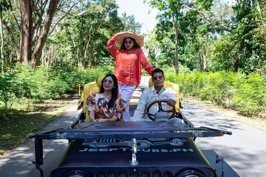A Jeep with three people, one driving and two passengers, on a road surrounded by greenery. 2