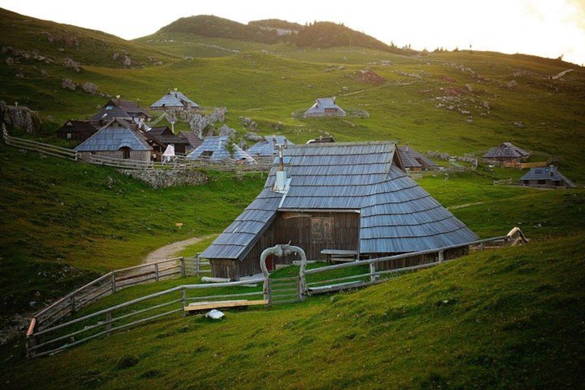 Eine ländliche Landschaft mit einem markanten Gebäude mit gewölbtem Dach, umgeben von kleineren Häusern und einem eingezäunten Bereich. 2