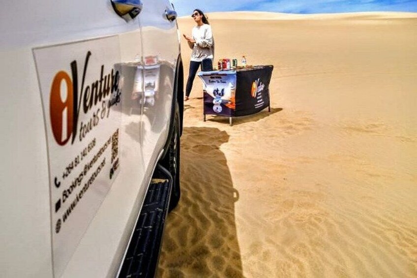 A desert scene with a white vehicle and a table with a sign that reads 'Venture Tours & Travel.' 4