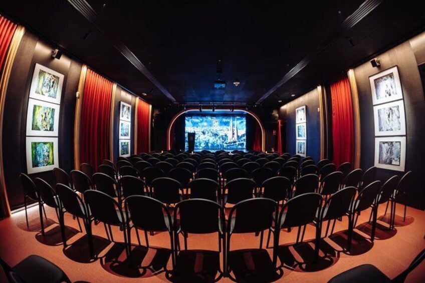 A theater with rows of black chairs, red curtains, and framed pictures on the walls. 2
