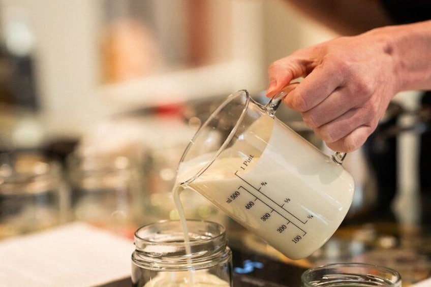 A hand pouring a white liquid from a measuring cup into a glass jar. 2