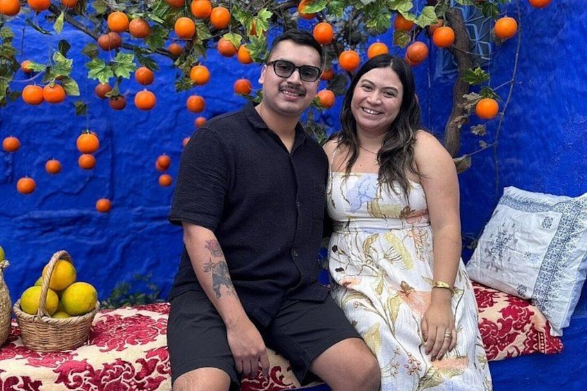 Un hombre y una mujer sentados en un sofá rojo y blanco con un fondo azul y fruta naranja colgando sobre ellos. 1