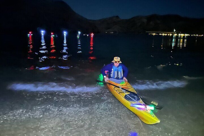 Una persona en kayak en una playa de noche con luces coloridas al fondo. 2