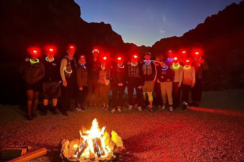 Un grupo de personas forman fila con linternas frontales, una fogata al frente y un paisaje montañoso al fondo. 4
