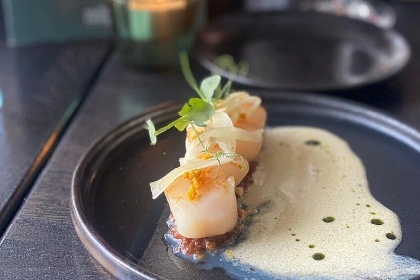 A plate with three scallops, a sauce, and some greens. 4