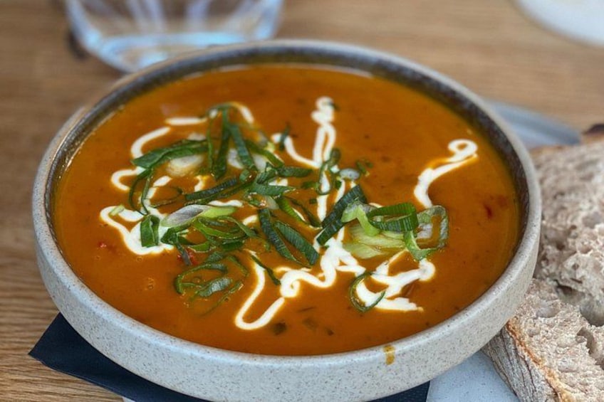 A bowl of soup with green garnishes and a drizzle of cream on a wooden table. 5