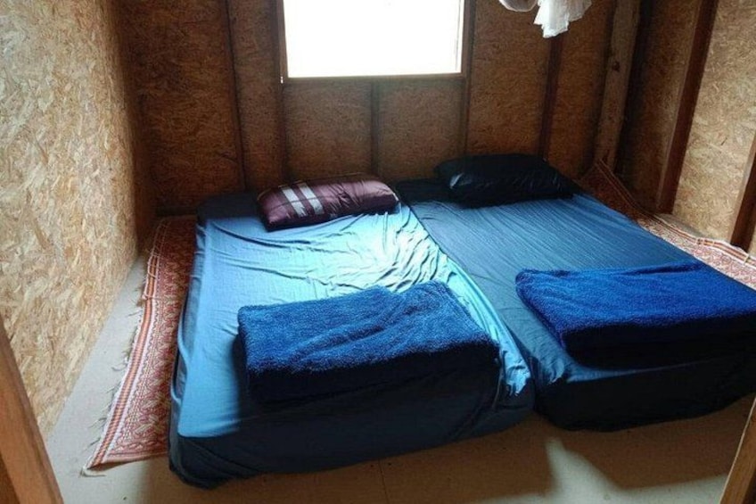 A small, cozy room with a single bed, a window, and a wooden wall. 1
