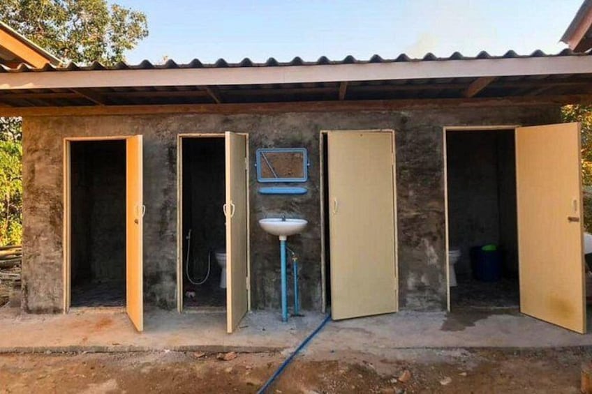 A rustic outdoor bathroom with three open doors, a sink, and a hose. 3