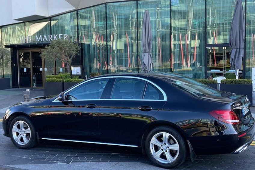 A black sedan parked in front of a building with a glass facade and the word 'MARKER' on the entrance. 1