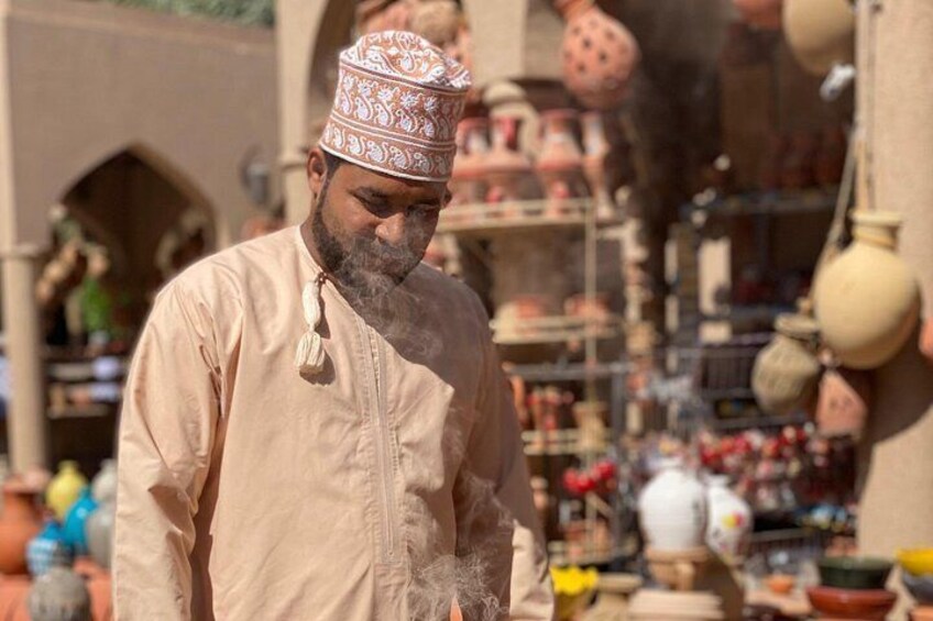 Eine Person in traditioneller Kleidung mit einer gemusterten Kappe steht vor einem Marktstand mit Tonwaren. 3