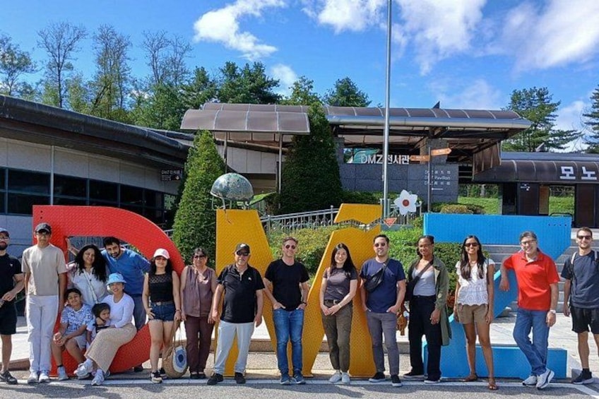 A group of people standing in front of a building with large colorful letters and a globe sculpture. 1