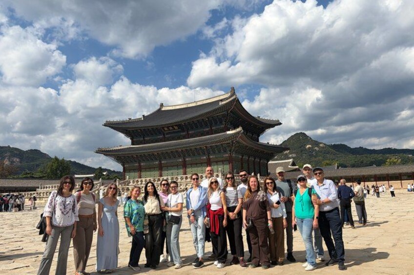 A group of people standing in front of a traditional Korean building with a mountainous backdrop. 2