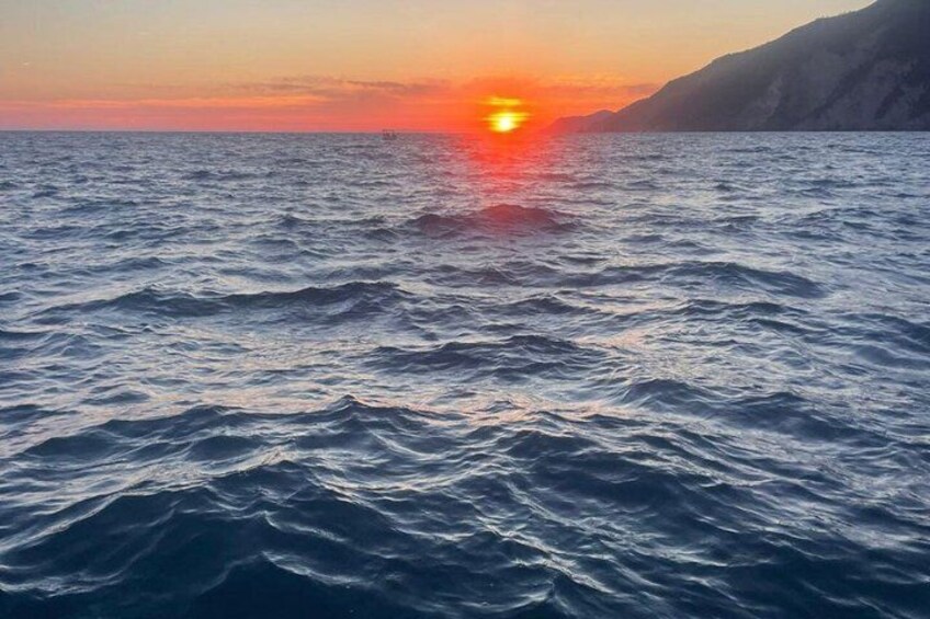 A sunset over the ocean with waves and a distant mountain. 5
