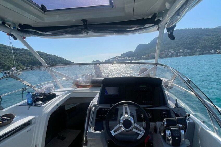 A boat's interior with a steering wheel, dashboard, and a clear view of the water and distant coastline. 3