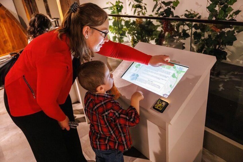 A woman and a child interacting with a digital kiosk in a museum or exhibition space. 4