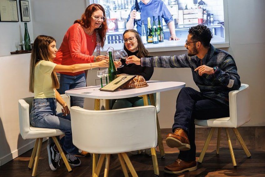 A group of people sitting around a table with wine bottles and glasses. 2