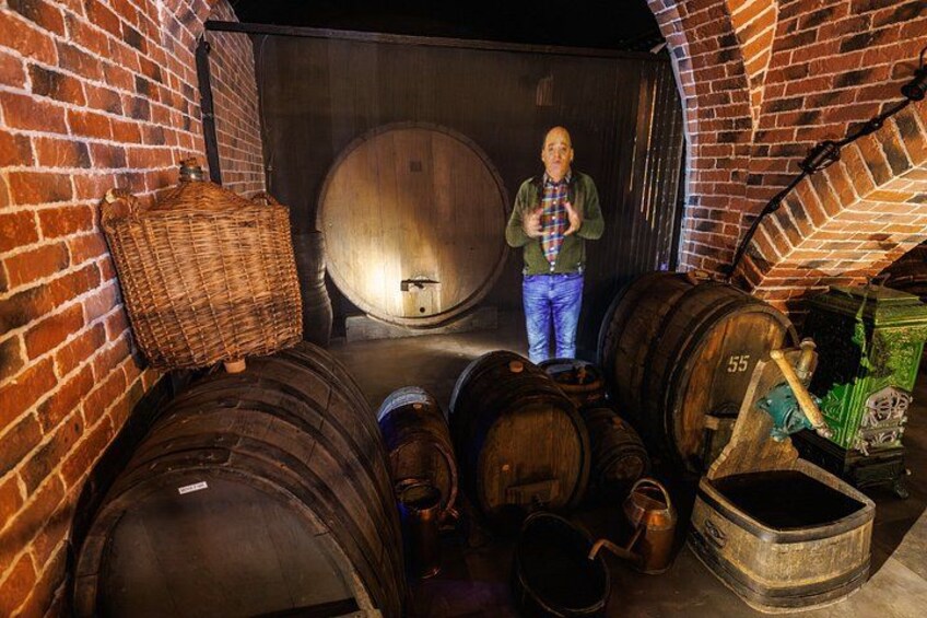 A person in a cellar with wooden barrels and a large wooden barrel in the background. 4
