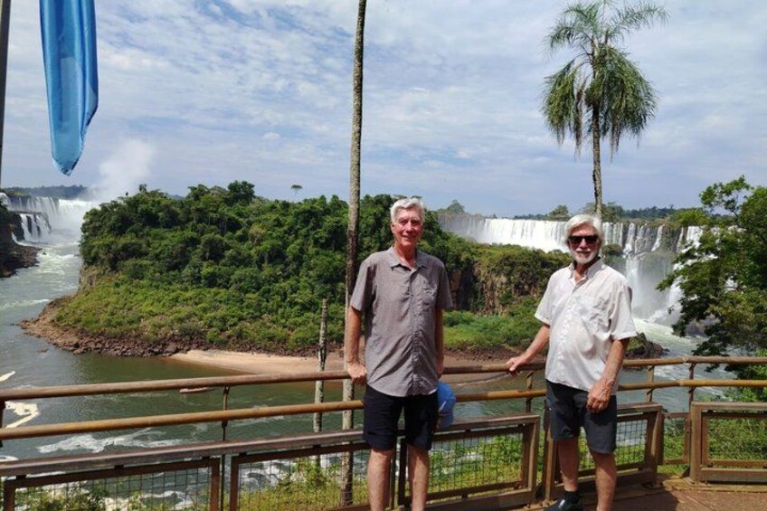 Dos personas de pie junto a una cascada con abundante vegetación y una palmera al fondo. 2