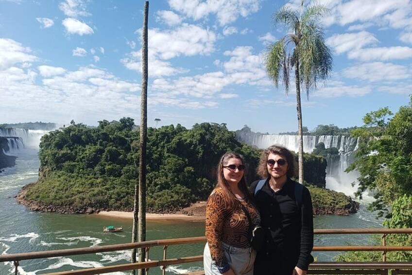 Dos personas de pie sobre un puente, con una cascada y abundante vegetación al fondo. 3