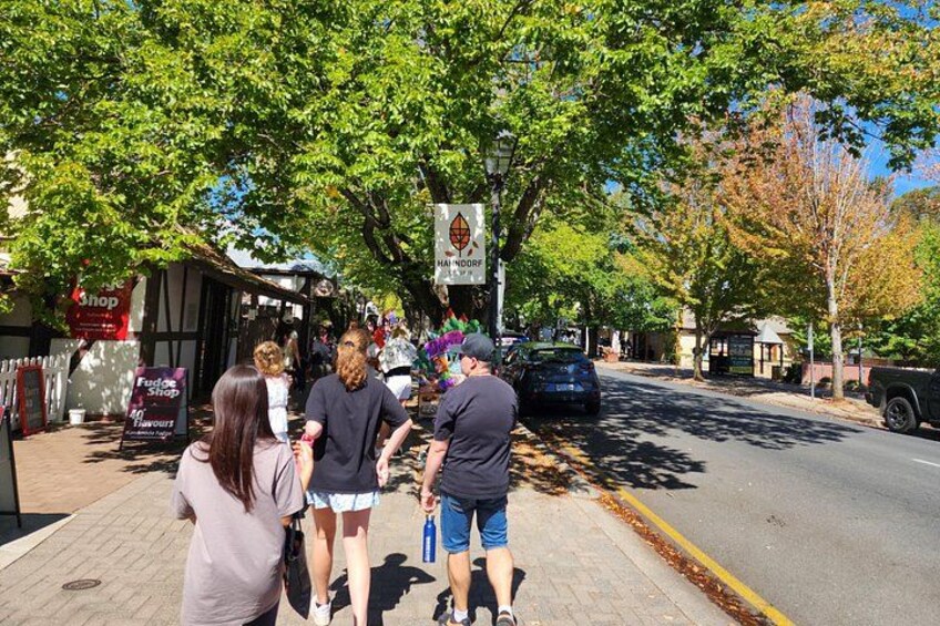 A street with pedestrians, a signboard, and parked cars. 2