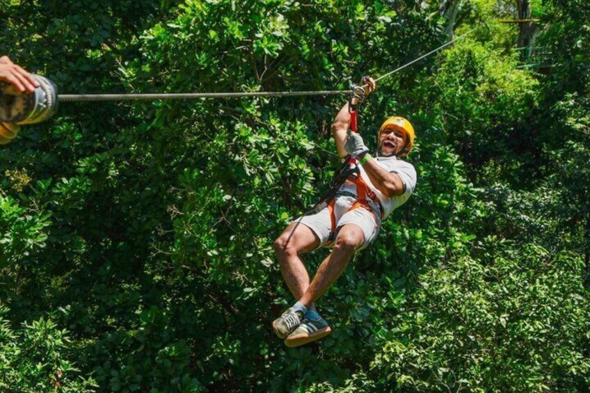 En person suser ned gennem en tæt skov på en zipline. 5