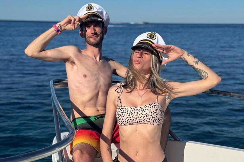 Two people on a boat, one wearing a captain's hat and the other a sailor's hat, with the ocean in the background. 2