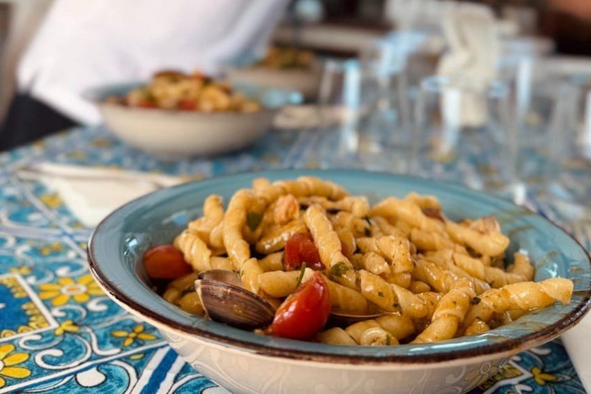A plate of pasta with cherry tomatoes and olives on a table with a blue and yellow patterned tablecloth. 5