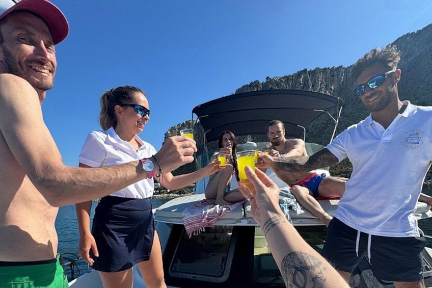 A group of people on a boat, some holding drinks, with a mountainous landscape in the background. 4