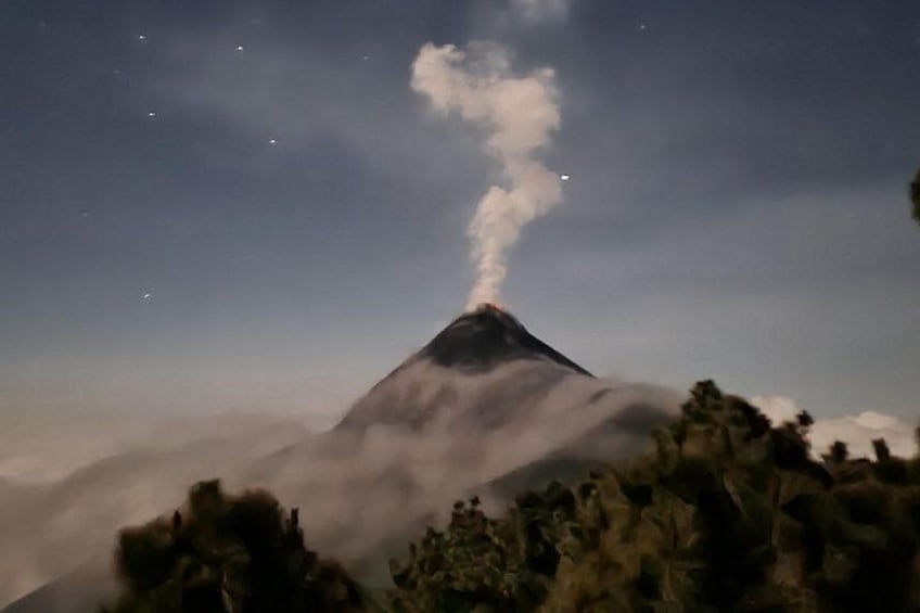 A volcano with smoke at its peak, surrounded by clouds and vegetation. 4