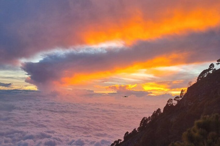 A sunset over a mountainous landscape with clouds and a plane in the distance. 2