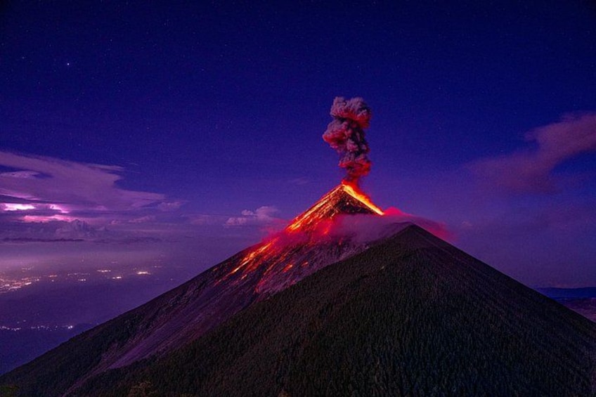A volcano with lava flowing down its side at night. 1