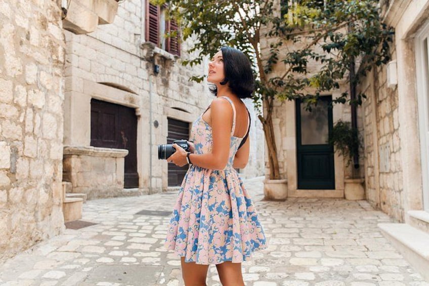 A woman in a floral dress standing in a stone-paved alley with buildings on either side. 5
