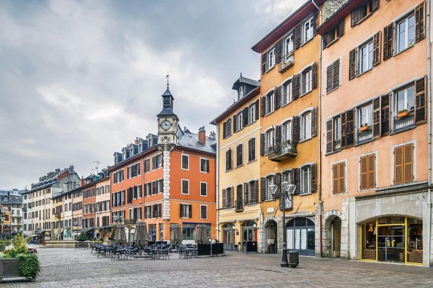 A cobblestone square with historic buildings, a clock tower, and outdoor seating. 1