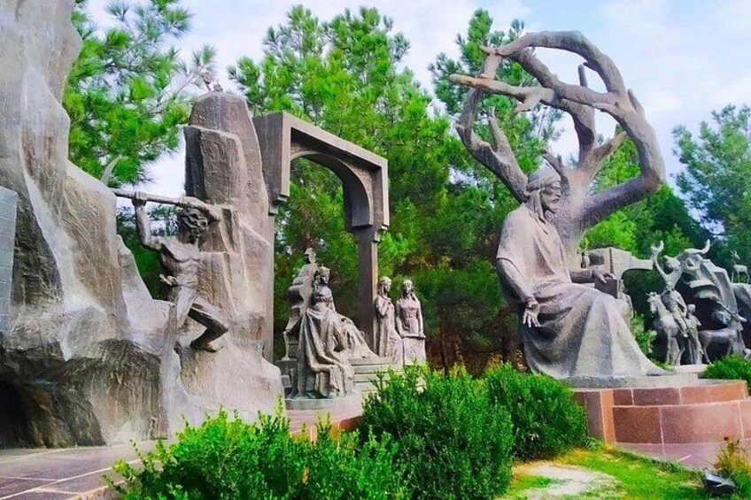 A sculpture garden with large stone statues, including a seated figure and a tree with branches. 2