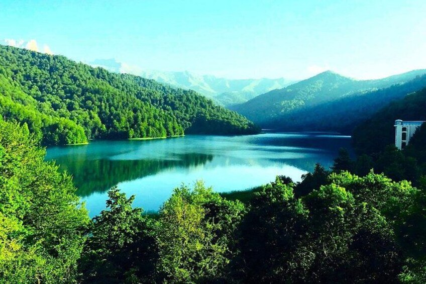 A lake surrounded by lush green hills and a small building on the right. 1